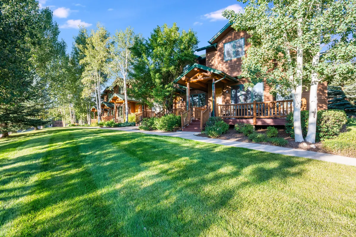 This image features the home's exterior with a well-manicured lawn, a wooden porch, and surrounding mature trees. The facade evokes a welcoming, family-friendly atmosphere and invites outdoor exploration and gatherings.