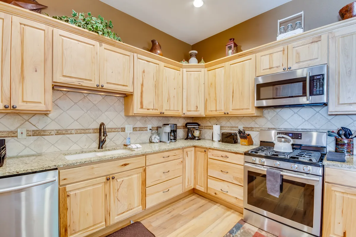 A welcoming kitchen with wooden cabinetry, granite countertops, stainless steel appliances, and decorative shelving. The space feels functional yet inviting, ideal for preparing meals or gathering for conversation over coffee.