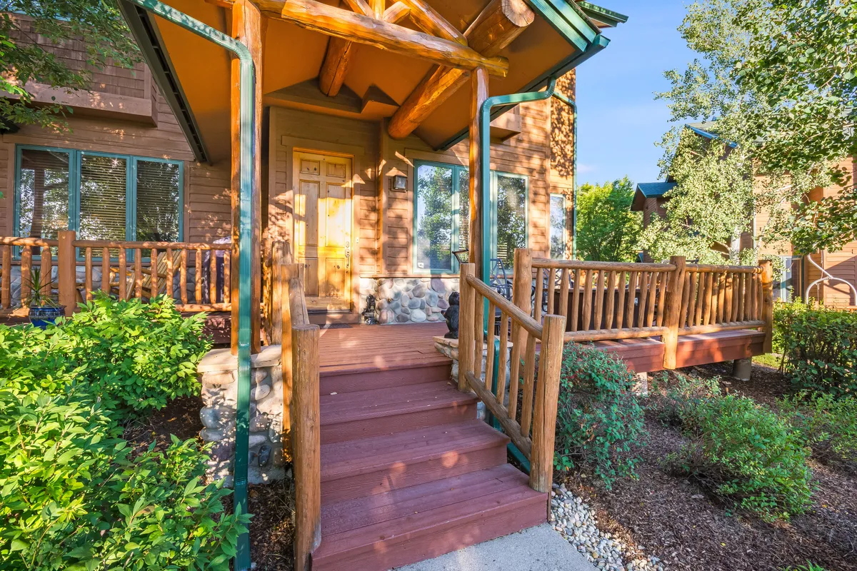This photo showcases the home's front entrance with wooden steps, log accents, and a landscaped garden. The inviting entry hints at the warm, comfortable spaces within and the welcoming vibe for guests and families arriving together.