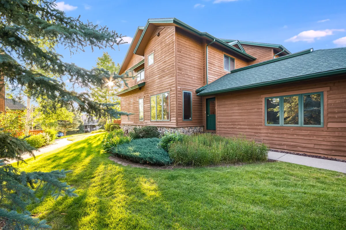 The image captures the wooden exterior of the home, large windows, a manicured lawn, and a landscaped garden. It highlights the seamless integration between indoor comfort and outdoor enjoyment, perfect for family gatherings and appreciating Steamboat’s natural surroundings.