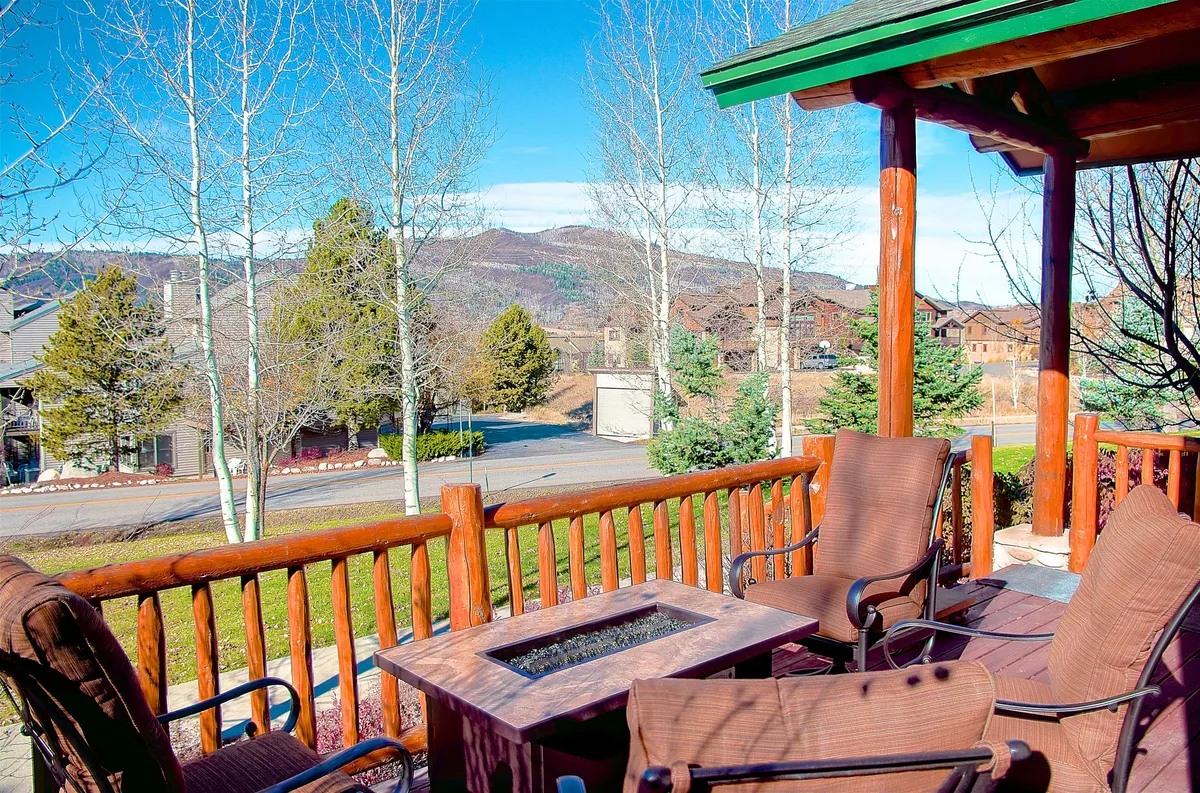 An exterior seating area with a wooden railing, fire pit, and comfortable outdoor seating. The vantage offers stunning views of the mountains, ideal for relaxing or socializing after a day outdoors.