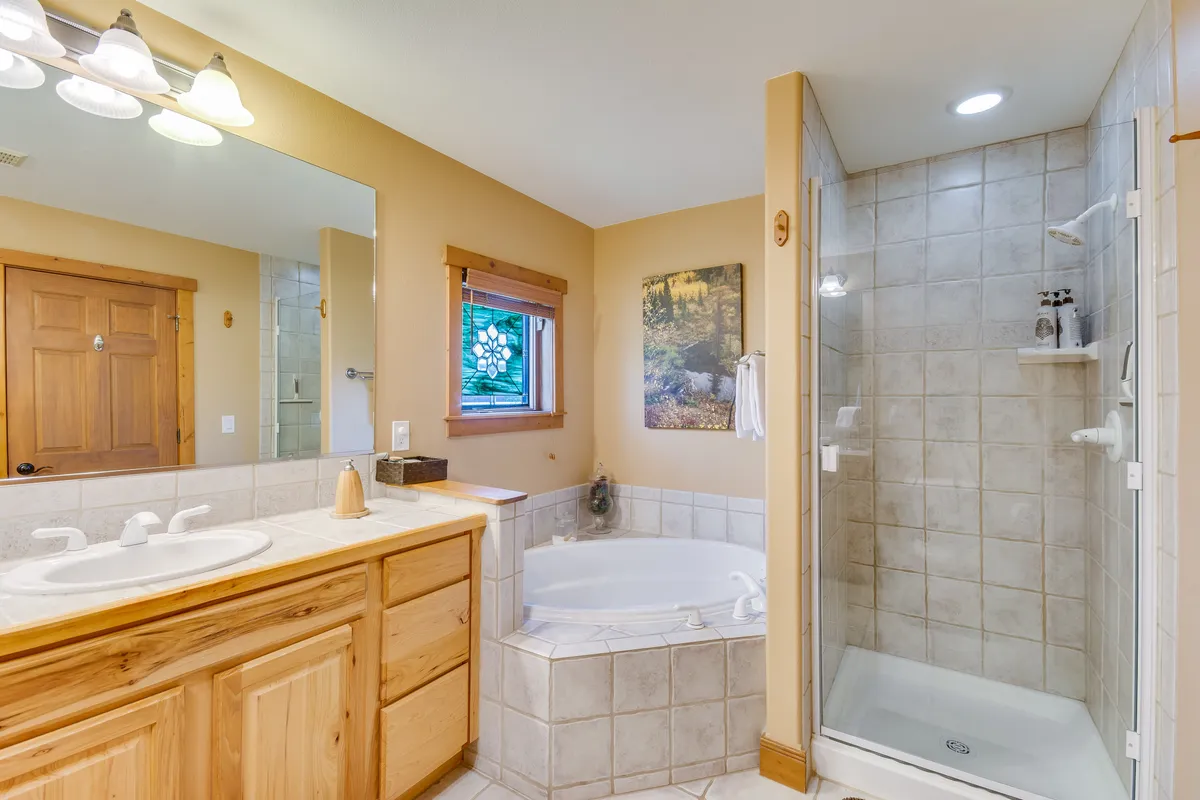 A calming bathroom scene with a bathtub, shower area, mirror, window that frames nature views, and tasteful wall art. The space feels serene and spa-like, ideal for rejuvenation after mountain adventures.