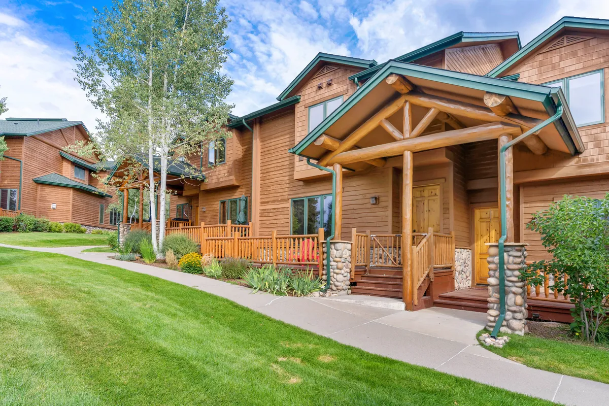 This exterior image highlights the inviting wooden entrance of the property, framed by stone accents and surrounded by a lush green lawn and landscaped shrubs. The porch area exudes warmth and connection to the outdoors, suggesting a welcoming spot to relax after a day downtown.