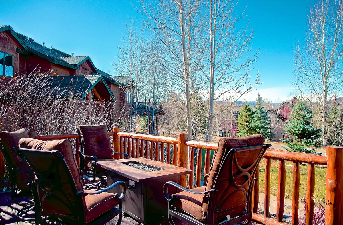 A cozy outdoor deck scene with comfortable seating clustered around a fire pit, all framed by mature trees and a wooden railing. The tranquil setting invokes feelings of relaxation after a day of adventure, with the fire pit as an inviting center for evening gatherings.